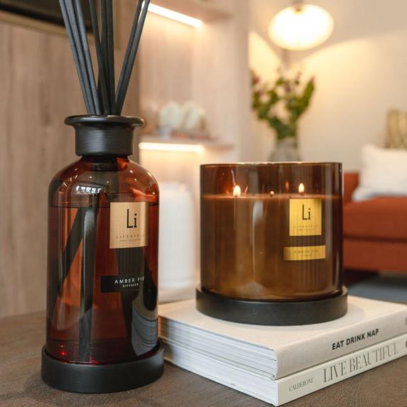A diffuser and a candle with 'Li' branding on a surface in a home setting.