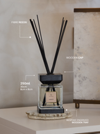 Diffuser with black reeds on a wooden tray against a neutral wall
