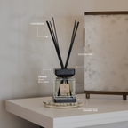 Diffuser with black reeds on a wooden tray against a neutral wall