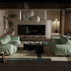 A modern living room featuring two oversized light green velvet sofas arranged symmetrically on a patterned rug in front of a minimalist fireplace.