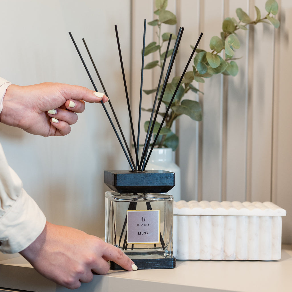 Person pointing at a diffuser with eucalyptus branches on a shelf.