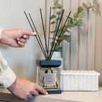 Person pointing at a diffuser with eucalyptus branches on a shelf.