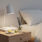 Lamp on a nightstand with a diffuser and lemon next to a bed