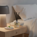 Diffuser on a nightstand next to a lamp and books with a blurred bed in the background
