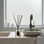 Bathroom setting with a diffuser bottle on a counter, sink, and window in the background.