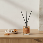 A diffuser bottle with black sticks on a wooden surface with a neutral background