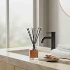 Diffuser with sticks on a bathroom counter with towels and faucet in the background