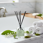A diffuser bottle labeled 'Tranquil' on a bathroom counter with towels and greenery.