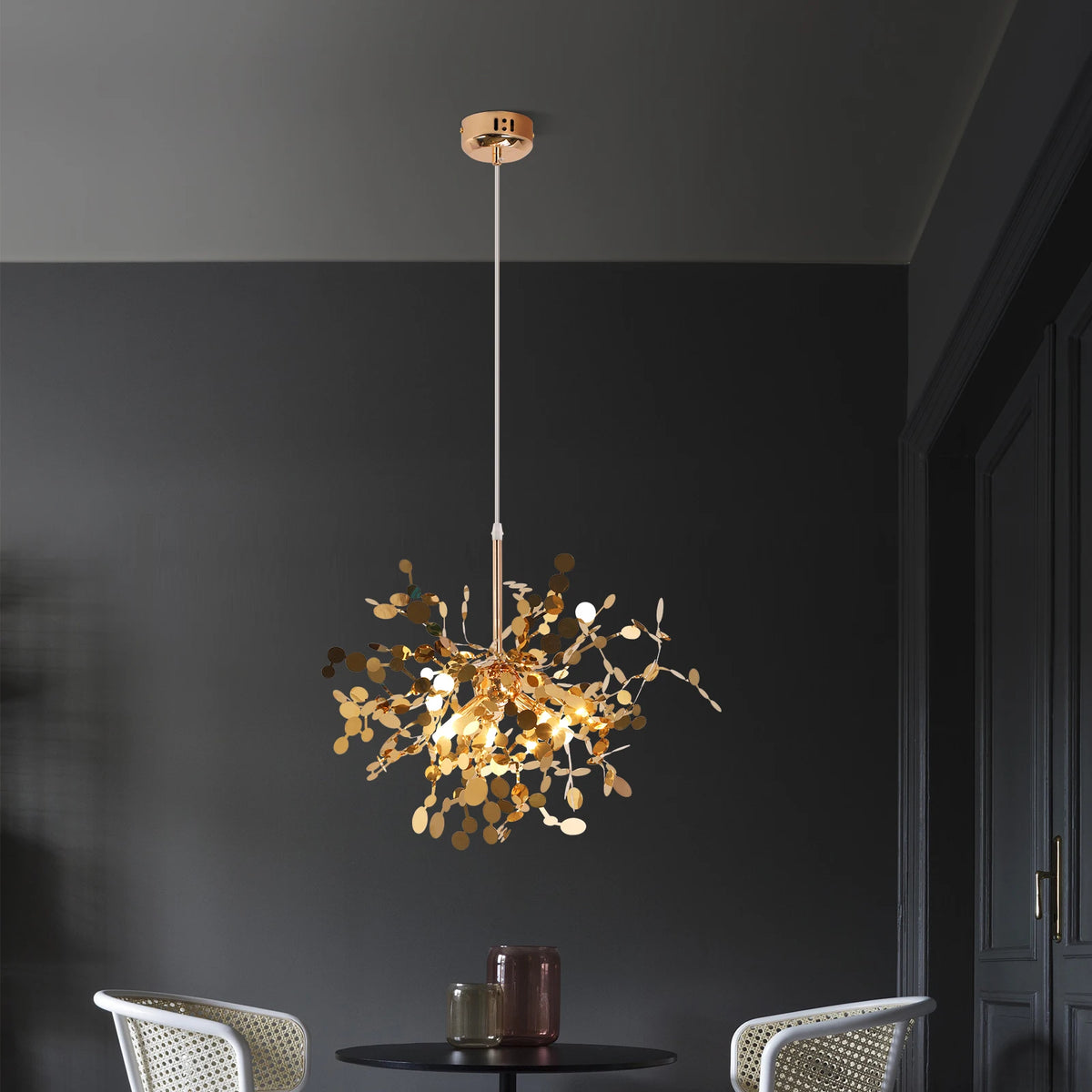 Gold chandelier hanging in a room with dark walls and a table.
