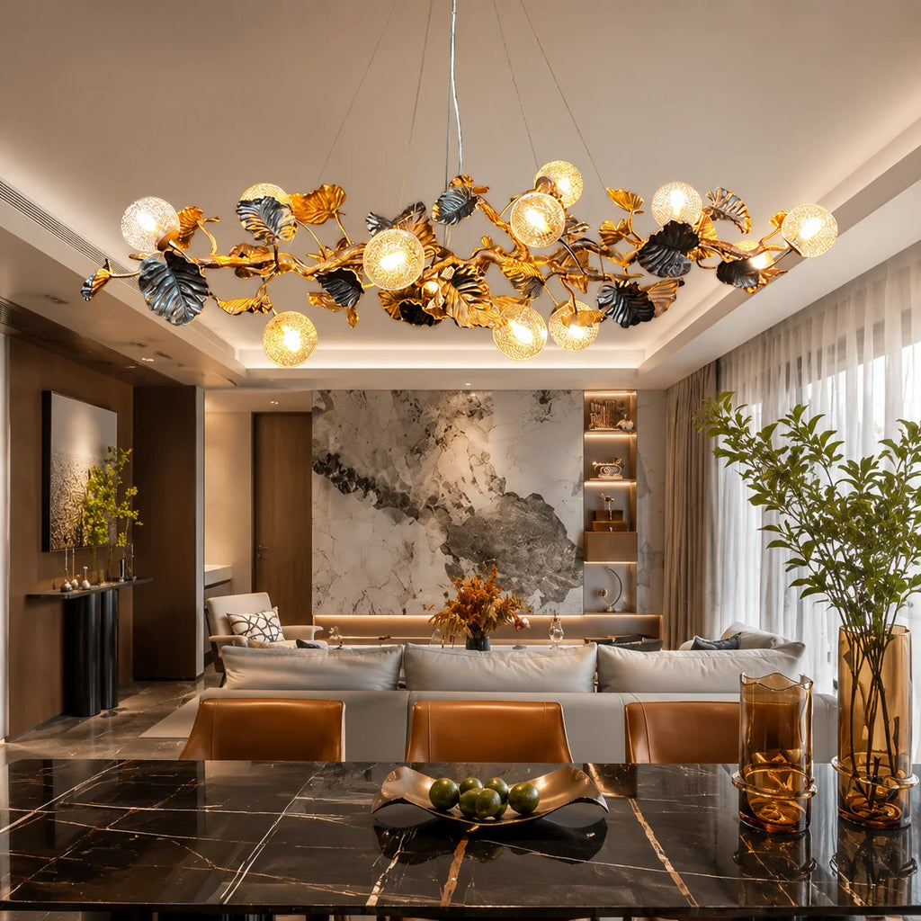 A large, ornate gold and black metal chandelier with multiple glowing globe bulbs hangs over a modern living room with a marble wall, sofa, and dark wood dining table in the foreground.
