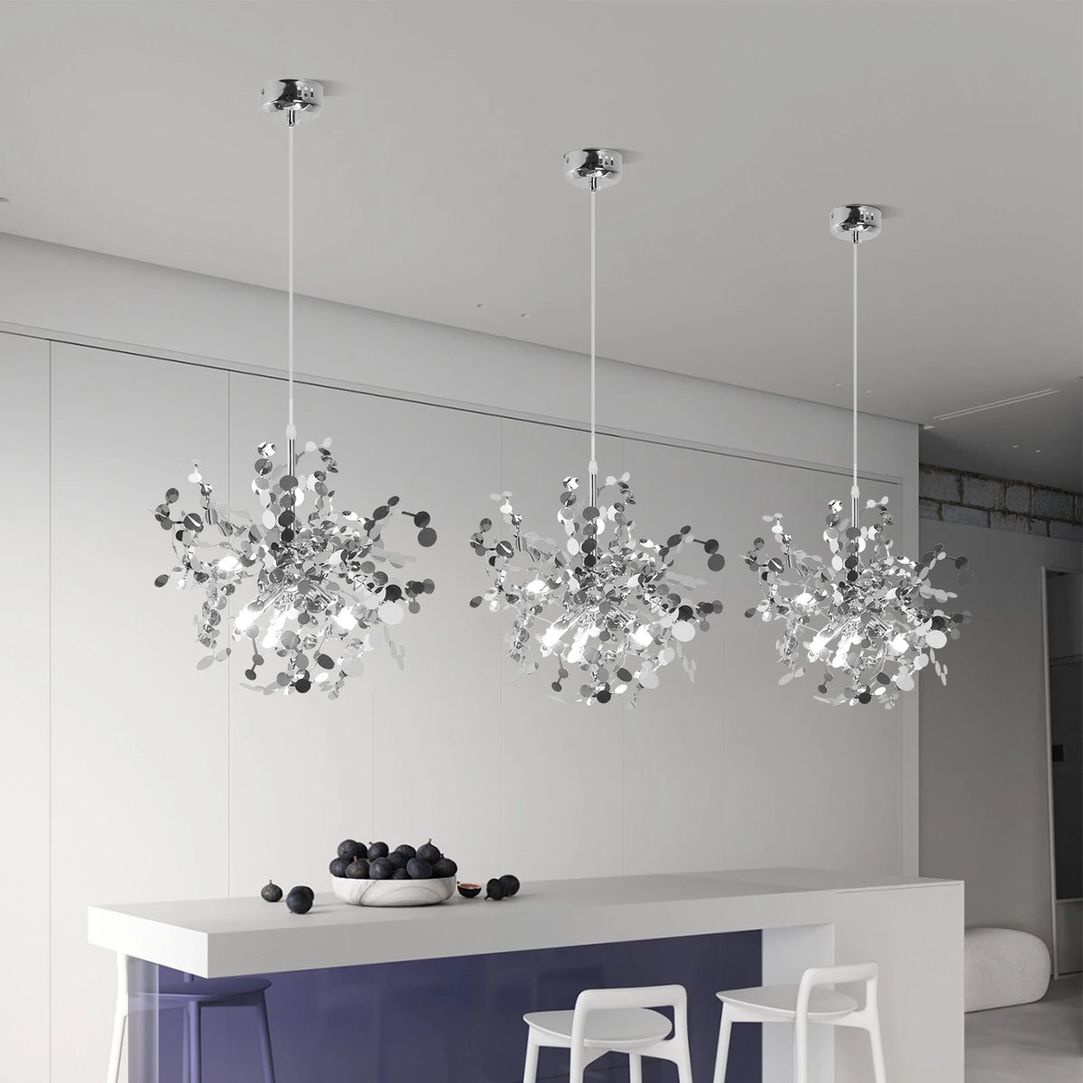 Three modern pendant lights hanging above a kitchen counter with fruit on a white wall background.