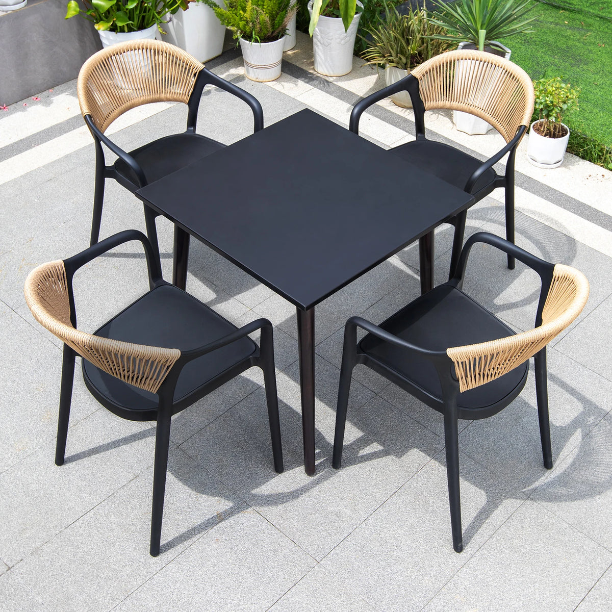 Outdoor dining set with black table and four chairs with wicker backrests on a patio.