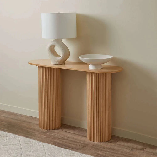 Wooden console table with a lamp and bowl against a beige wall.