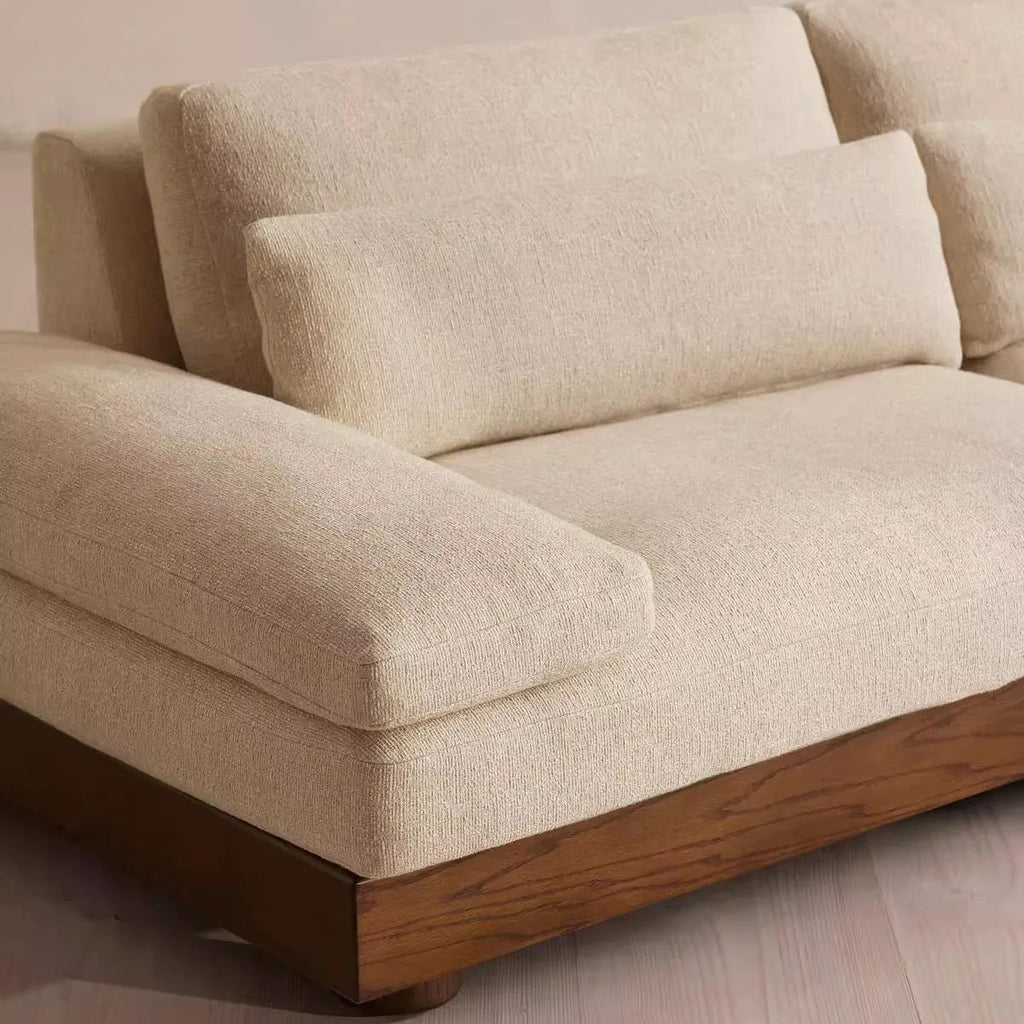 Beige sofa with wooden legs on a light wooden floor.