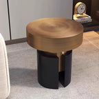A modern round side table with a brushed brass top and a split black metal base, shown in a styled interior setting.