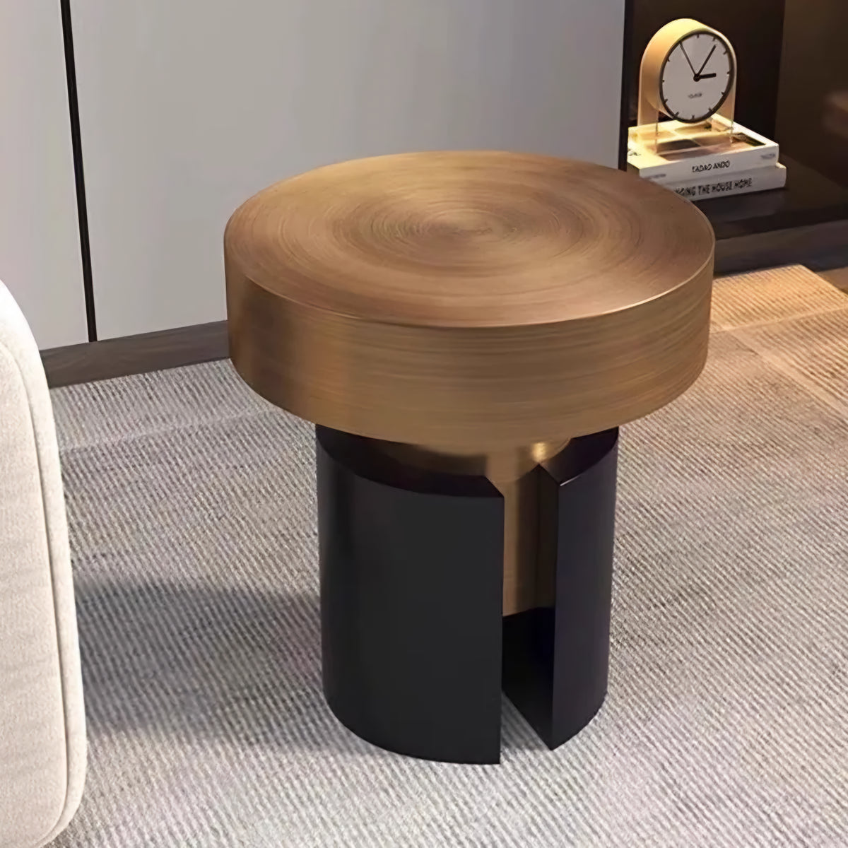 A modern round side table with a brushed brass top and a split black metal base, shown in a styled interior setting.