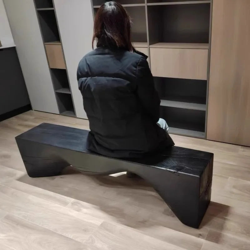 Person sitting on a modern black bench in a minimalistic room.