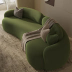 Green sofa with a blanket and pillow in a room with a window and light-colored carpet.