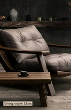 A modern lounge chair with a tufted taupe-gray cushion and dark wood frame, shown in a styled interior setting with a wooden coffee table and a text overlay indicating a sitting height of 38cm.