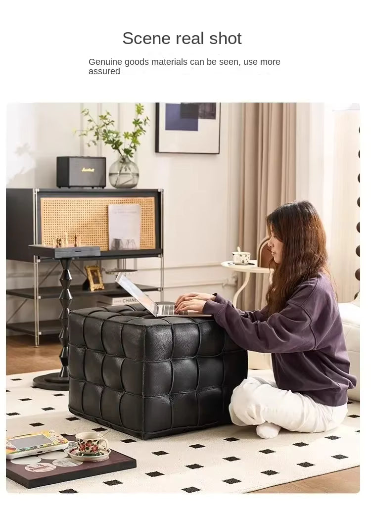 Woman using a laptop on a black leather ottoman in a modern living room.