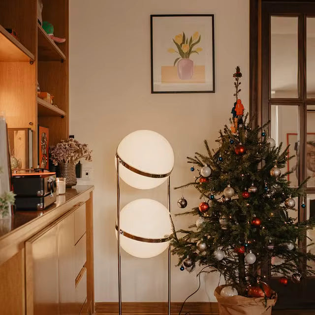 Decorative indoor Christmas tree with lights and ornaments in a room with a lamp and framed picture on the wall.