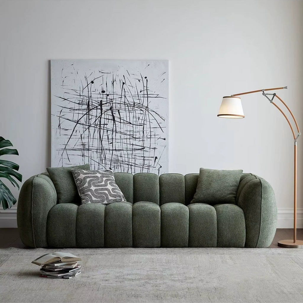 Green sofa in a living room with abstract art and a lamp.