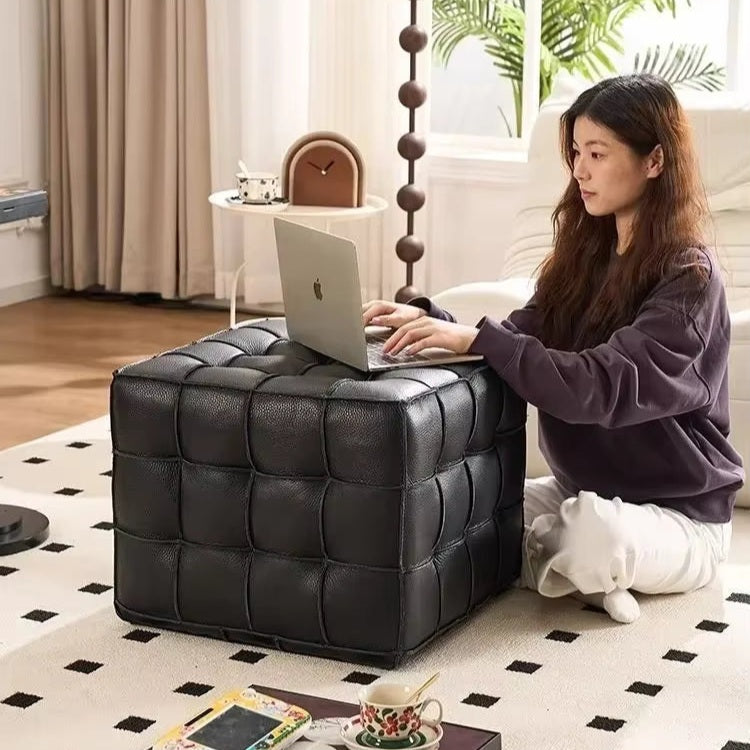 Woman using a laptop on a black cube ottoman in a home setting