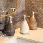 Three decorative soap dispensers on a bathroom counter with a mirror in the background.