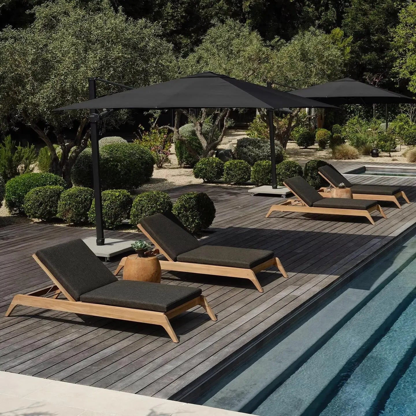 Outdoor lounge chairs with black cushions and umbrellas by a pool