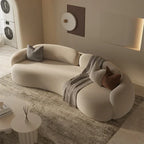 Modern beige sofa with decorative pillows and a blanket in a living room setting.