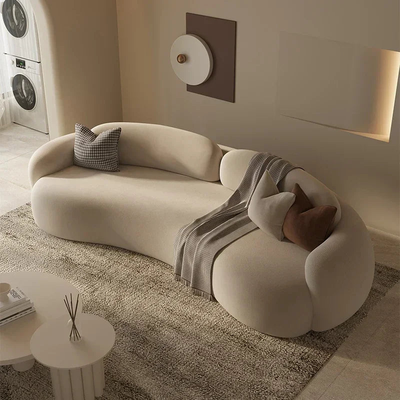 Modern beige sofa with decorative pillows and a blanket in a living room setting.