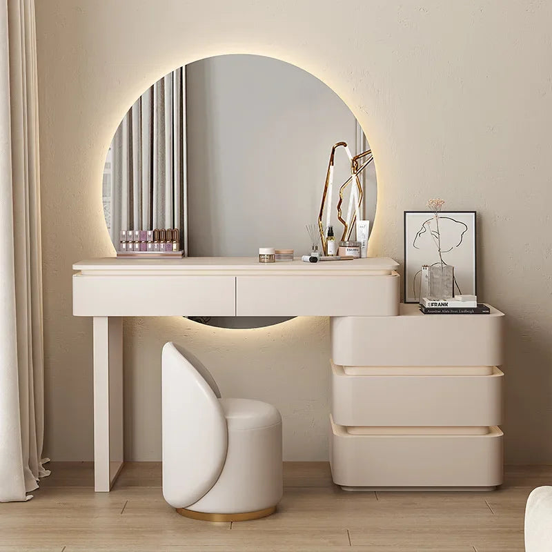Modern vanity setup with round mirror, desk, and chair in a well-lit room.