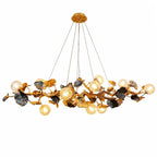 A modern multi-light chandelier with a gold-toned metal branch structure, dark textured leaf accents, and multiple clear glass globe bulbs, shown against a plain white background.
