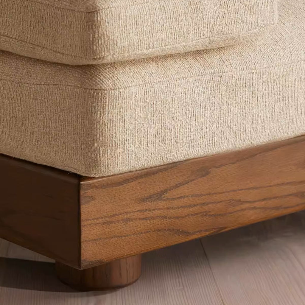 Close-up of a beige textured upholstered sofa corner with a medium brown wooden base and leg, shown on a light wood floor.