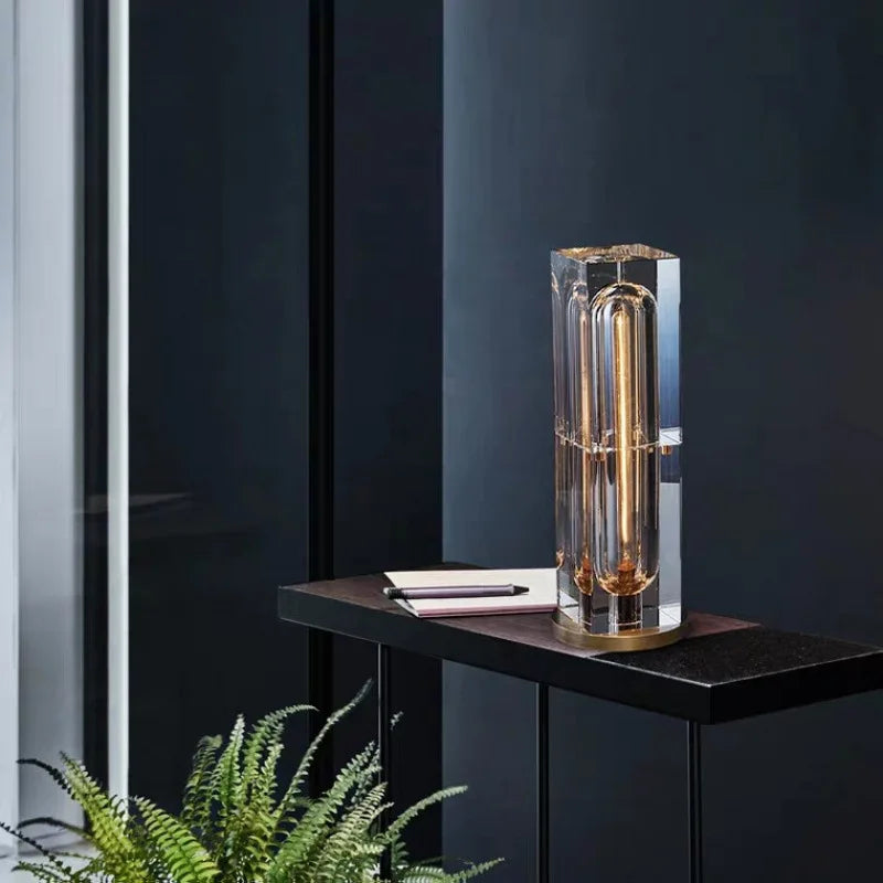 Modern table lamp with clear glass shade on a dark surface against a black wall.