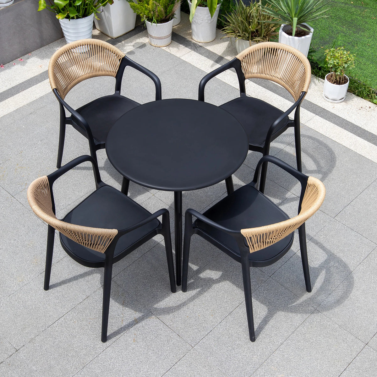 Outdoor patio set with black table and four chairs with wicker backrests on a tiled patio.