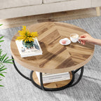 Round wooden coffee table with a hand holding a cup, books, and a plant in a living room setting.
