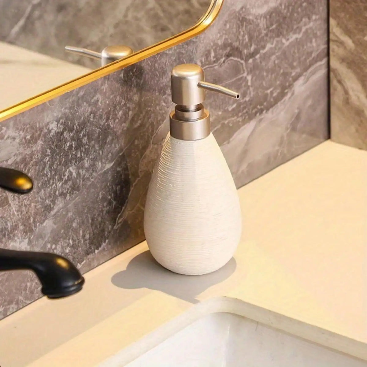White ceramic soap dispenser on a bathroom counter with marble wall and mirror.