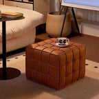 Brown leather ottoman in a living room setting with a coffee cup and saucer on top.