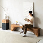 Woman sitting on a wooden bench reading a book in a minimalistic room.