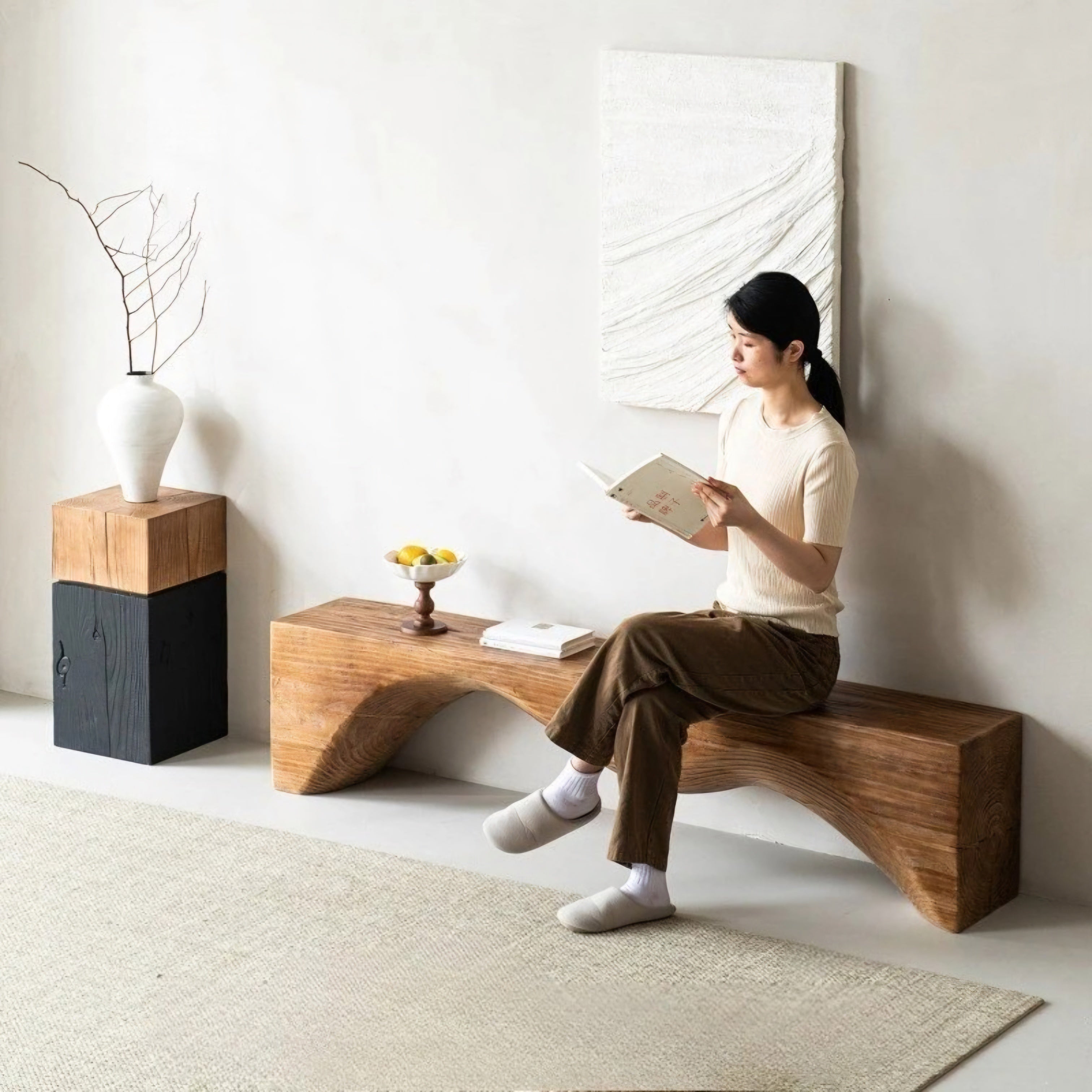 Woman sitting on a wooden bench reading a book in a minimalistic room.