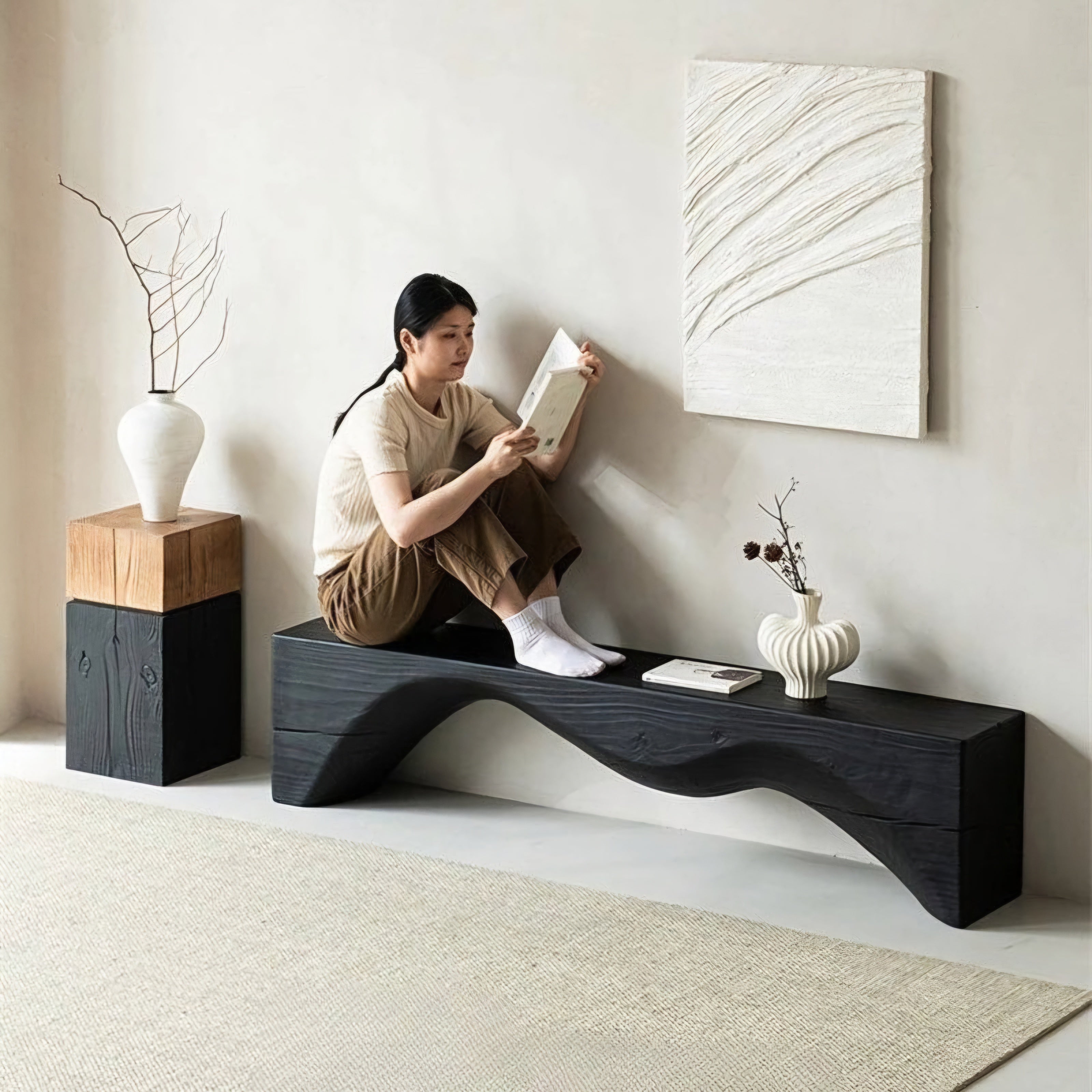 Woman reading a book on a modern black bench in a minimalistic room.