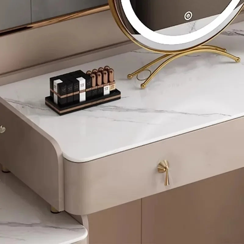 Beige vanity table with a marble top and a round mirror with lights on a white floor.