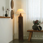 Decorative floor lamp with wooden base and shade in a room with a window and wall art.