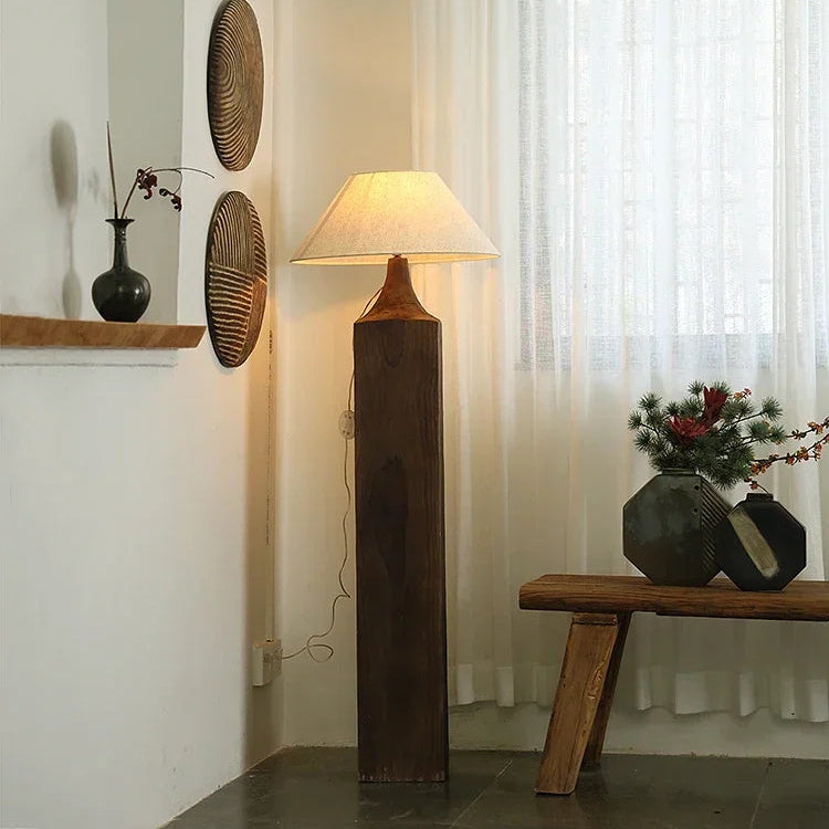Decorative floor lamp with wooden base and shade in a room with a window and wall art.