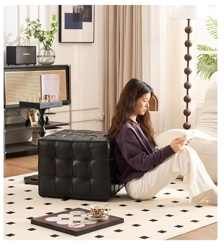 Woman sitting on a black cube-shaped ottoman in a stylish living room.