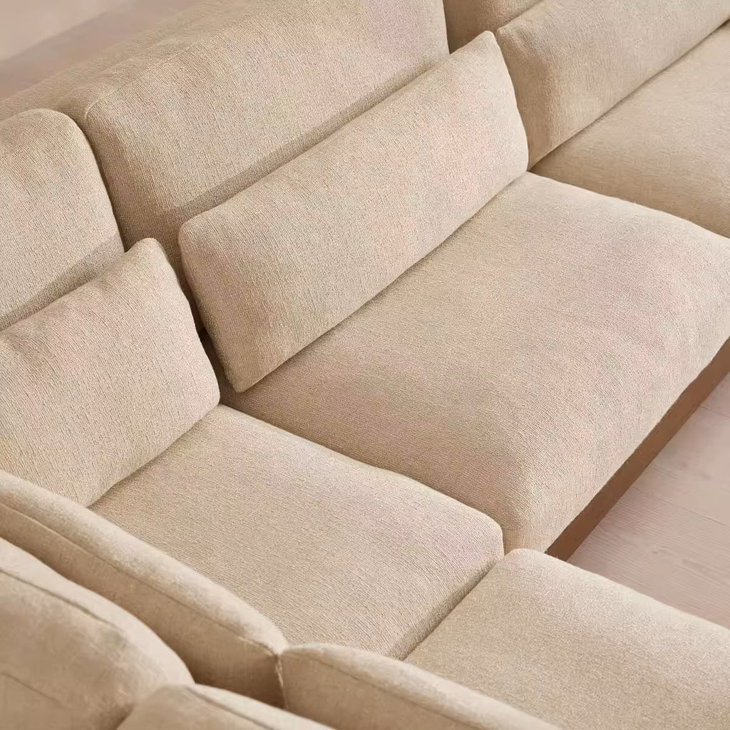 Beige textured fabric sectional sofa with multiple plush seat and back cushions, shown in a close-up interior view.