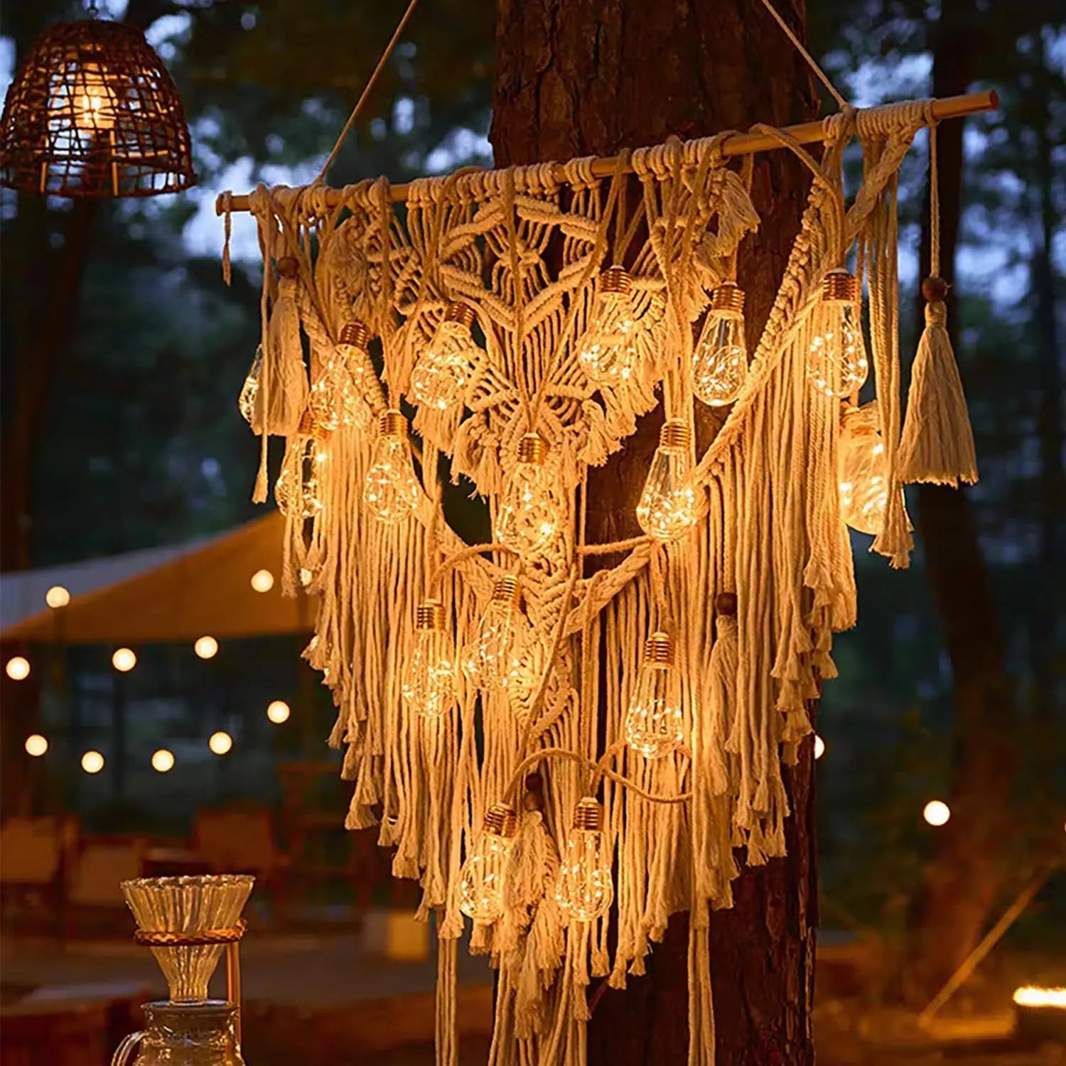 Macrame chandelier with string lights hanging from a tree in an outdoor setting.
