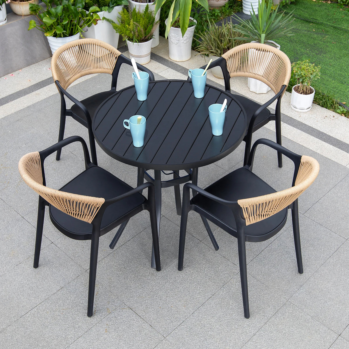 Outdoor patio set with black table and four chairs with woven backrests on a tiled patio.