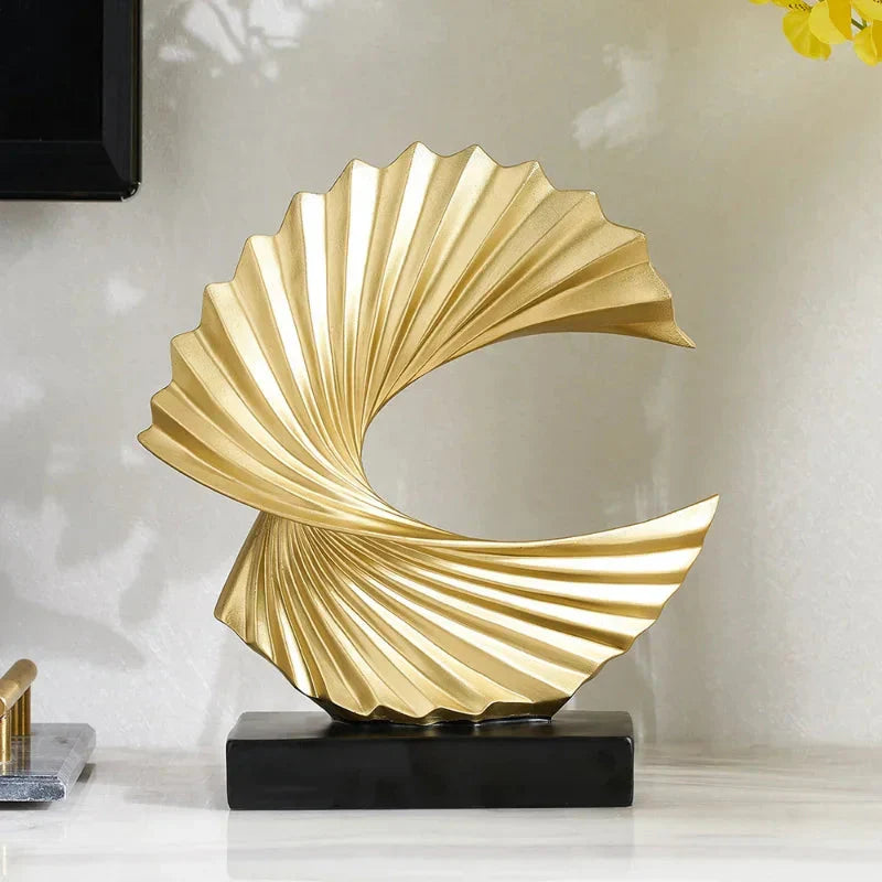 Gold decorative sculpture on a black base against a light wall.